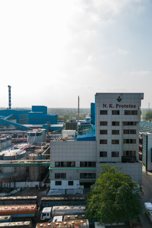 Aerial view of N. K. Proteins industrial building and factory complex with tanks, pipelines, and trucks parked in front